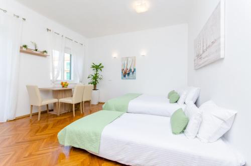 zwei Betten in einem weißen Zimmer mit einem Tisch in der Unterkunft Apartment ''Pomalo'' in Split
