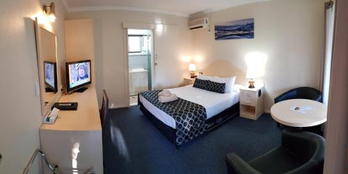 um quarto de hotel com uma cama, uma secretária e uma televisão em Amber Court Motor Inn em Coonabarabran