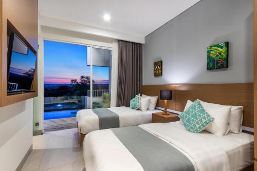zwei Betten in einem Hotelzimmer mit großem Fenster in der Unterkunft Villa Melati R3 Ungasan in Uluwatu