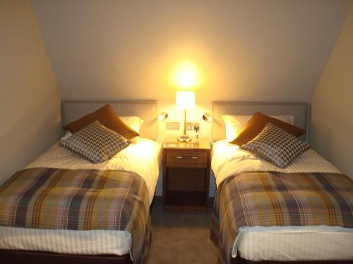 a room with two beds and a night stand with a lamp at Cruachan Hotel in Fort William