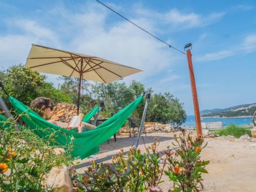 a woman sitting in a hammock under an umbrella on the beach at Hostel Kapa in Hvar