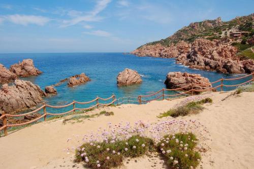 a beach with rocks in the water and a fence at Casa Magda in Costa Paradiso
