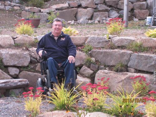 a man in a wheelchair sitting in a garden at Gîte Vita Bella B&B in Saint Adolphe D'Howard