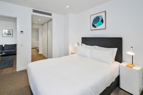 a bedroom with a large white bed and a living room at Anchorage Apartments Hampton in Melbourne