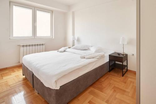 a white bedroom with a large bed and a wooden floor at Smart Apartments in Skopje