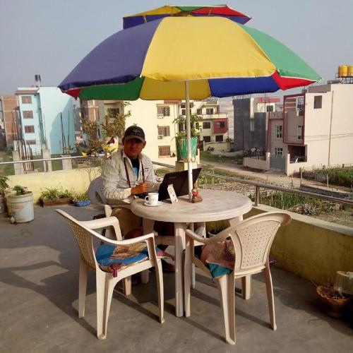 a woman sitting at a table under an umbrella at Everest Home Stay Apartment in Pātan