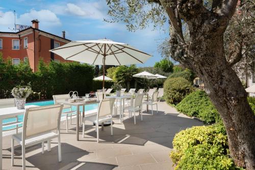 a row of tables and chairs with an umbrella at Vialeromadodici Rooms & Apartments in Lazise