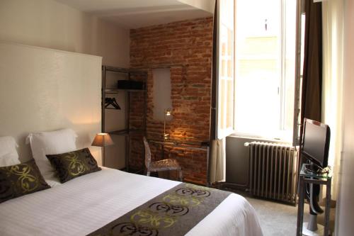 a bedroom with a bed and a brick wall at Hôtel des Arts in Toulouse