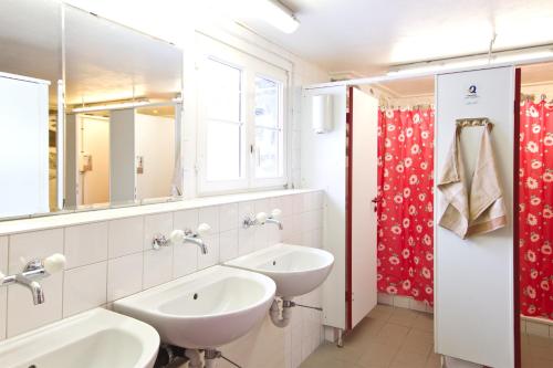 a bathroom with two sinks and a red shower curtain at Mountain Hostel Gimmelwald in Gimmelwald