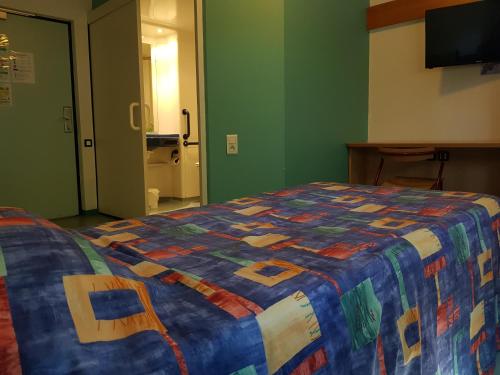a bed with a colorful quilt on it in a room at ETHIC ETAPES DIJON Accueil 24h24 et parking gratuit in Dijon