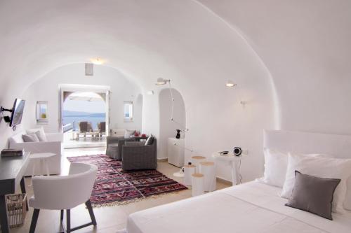a white bedroom with a bed and a living room at Santorini Secret Suites & Spa, Small Luxury Hotels of the World in Oia