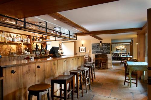 a bar in a restaurant with wooden walls and stools at The Museum Inn in Farnham