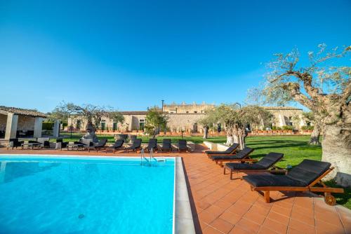 a swimming pool with chaises and chairs next to a building at Torre Don Virgilio Country Hotel in Cannizzara