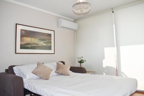 a white bedroom with a bed and a chandelier at Kennedy Dream Apartment in Santiago
