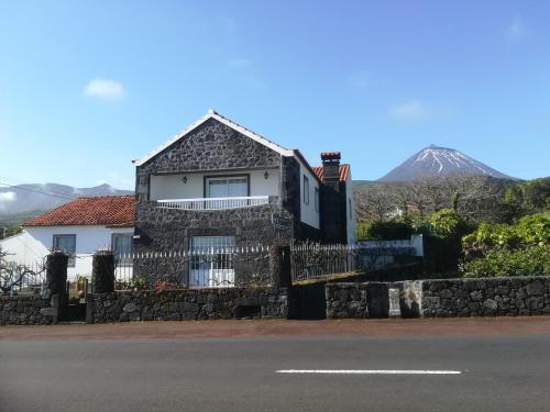 a house with a stone fence and a mountain in the background at Alojamentos A Buraca in São Roque do Pico