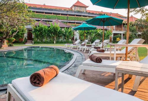 a pool with chairs and umbrellas next to a resort at Astagina Resort Villa and Spa in Legian