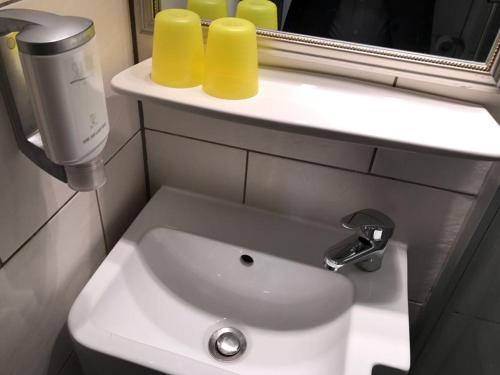 a bathroom sink with two yellow cups on a shelf at Balthasar Neumann Speiserei & Gästehaus - Zentrum Brühl -E-Ladestation, nähe Phantasialand in Brühl