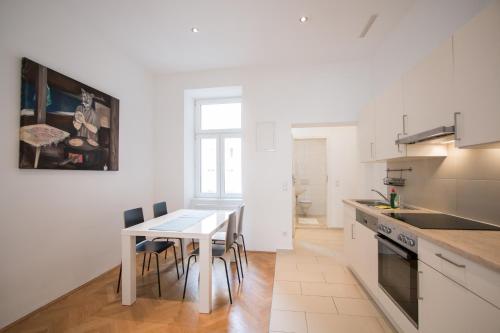 eine weiße Küche mit einem Tisch und Stühlen in der Unterkunft Porzellangarten Apartment I contactless Check-In in Wien