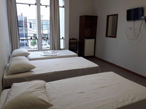 three beds in a room with a large window at Hotel Danubio in Itabaiana