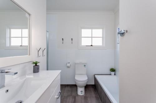 a white bathroom with a toilet and a tub and a sink at Bay Cottage in Sorrento