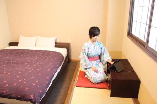 a woman in kimono sitting on the floor next to a bed at K's House Takayama Oasis [2nd K's Hostel] in Takayama