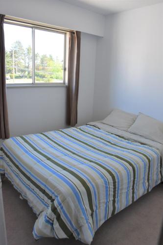 a bed with a striped blanket in a room with a window at North Coast Trail Backpackers Ltd in Port Hardy