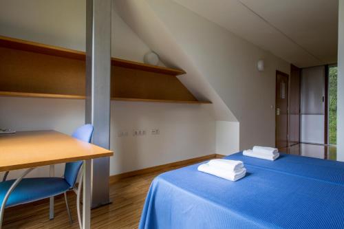 Cette chambre comprend un lit bleu, une table et des chaises. dans l'établissement Residencia Universitaria O Castro, à Vigo