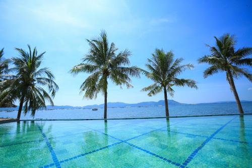 a swimming pool with palm trees in front of the ocean at Que Toi Village Resort Phu Yen in Song Cau