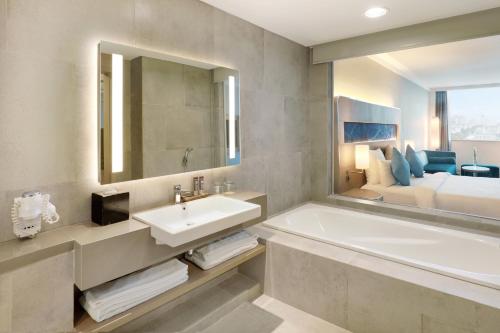a bathroom with a tub and a sink and a bed at Novotel Jakarta Mangga Dua Square in Jakarta