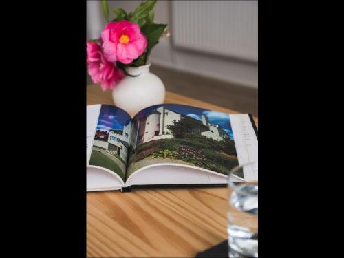 a book on a table with a glass of water and a flower at Cedar Apartment in Helensburgh