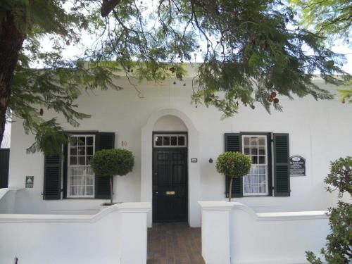 a white house with black shuttered windows and a door at De Kothuize 10 in Graaff-Reinet