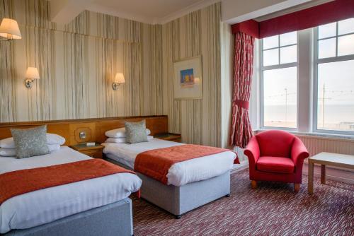 Una habitación de hotel con dos camas y una silla roja. en Cliffs Hotel, en Blackpool