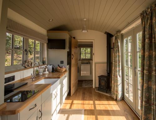 a kitchen with white cabinets and wooden floors and windows at Luxury Shepherds Hut in Bransgore