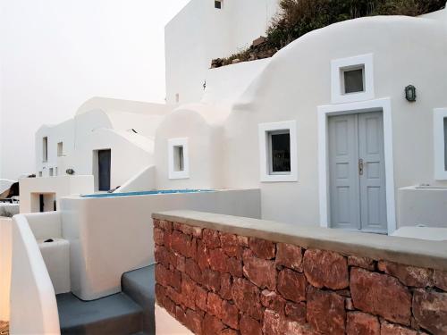 a white house with a brick wall and a door at Aqua & Terra Traditional Cave Houses in Oia