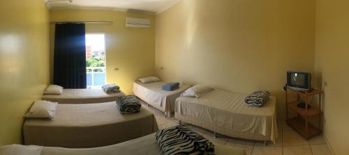 a room with three beds and a tv and a window at Hotel Via Sacra in Trindade