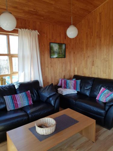 ein Wohnzimmer mit einem schwarzen Ledersofa und einem Tisch in der Unterkunft Ekra Cottages in Lagarfljótsvirkjun