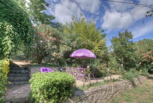 a purple umbrella in a garden with chairs and trees at A Pivarella in Grosseto-Prugna