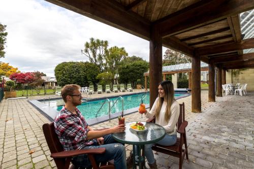 Un uomo e una donna seduti a un tavolo vicino a una piscina di Distinction Te Anau Hotel & Villas a Te Anau