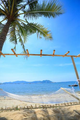 a hammock on a beach with a palm tree and the ocean at Que Toi Village Resort Phu Yen in Song Cau