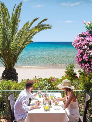 a man and woman sitting at a table on the beach at Forte Village Resort - Le Palme in Santa Margherita di Pula
