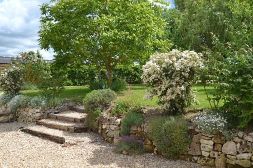 a garden with a stone wall and a tree and flowers at les gîtes de l'argenterie à 15km du zoo de Beauval classés 4 étoiles in Fontguenand