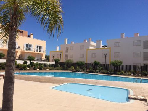 a swimming pool with a palm tree and buildings at Casa Cabanas - Cabanas Gardens in Cabanas de Tavira