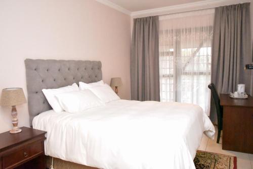 a bedroom with a large white bed and a window at Vinolux Guest House in Mthatha