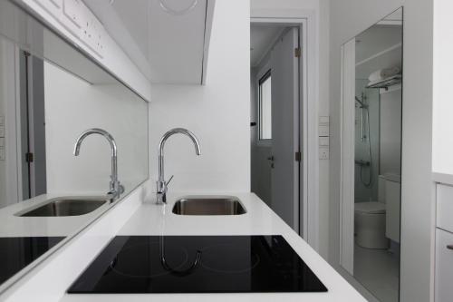 a white kitchen with two sinks and a mirror at The White Pearl Suite - beach front city centre with sea view. in Limassol