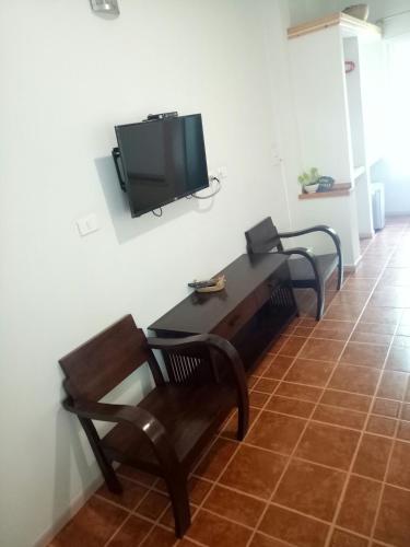 a living room with a bench and a tv on the wall at Baan Jaru in Chiang Rai