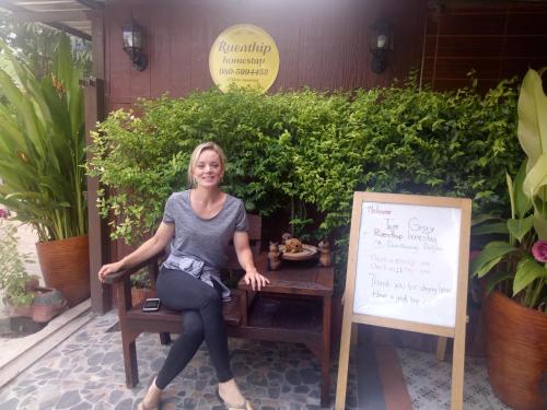 a woman sitting on a bench next to a sign at Ruenthip Homestay in Bangkok
