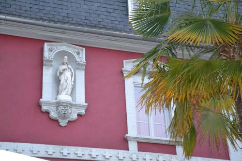 a statue on the side of a pink building at Hôtel Acropolis - Lourdes in Lourdes