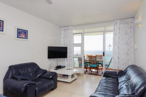 a living room with a black leather couch and a television at Chakas Cove 94 in Ballito