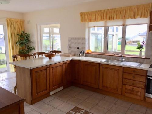 a kitchen with wooden cabinets and a sink and windows at Sheila's View - Spanish Point, Co. Clare in Spanish Point