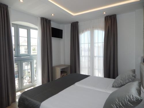 a bedroom with a large white bed and windows at Hostal Boutique Doña Carmen - Adults Recommended in Nerja